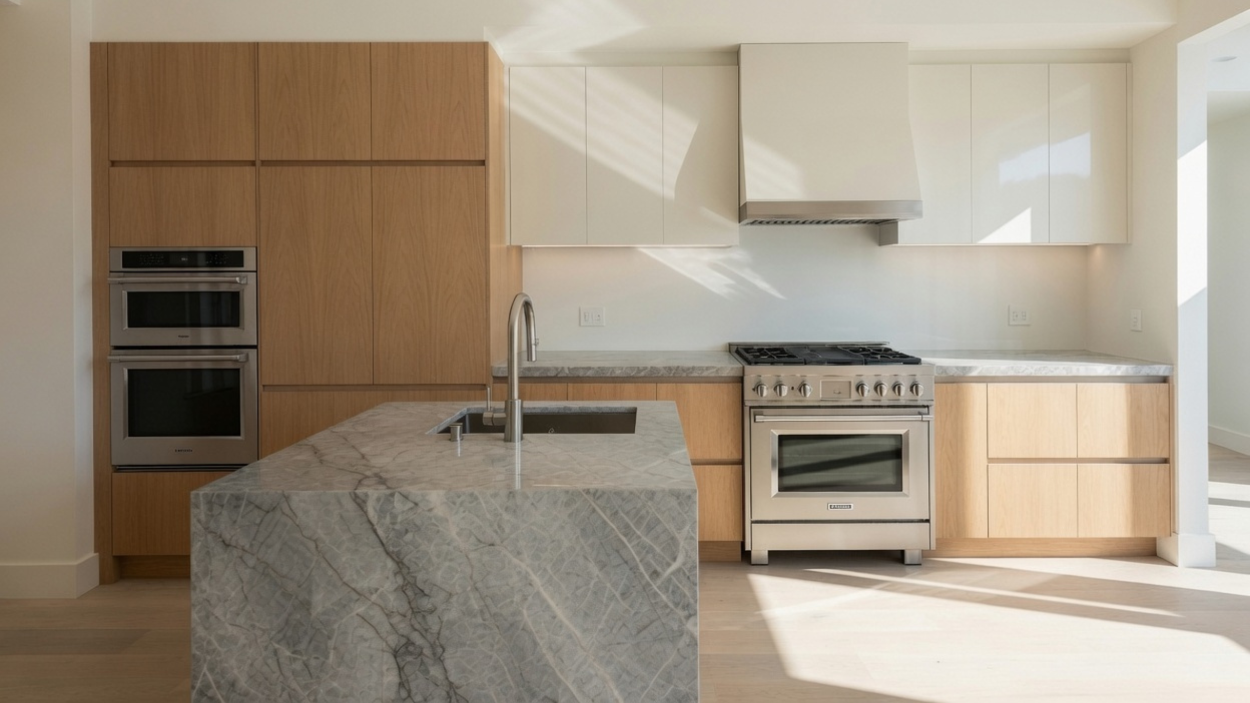 Minimal kitchen with light oak cabinets, warm white upper cabinets and a gray stone island.