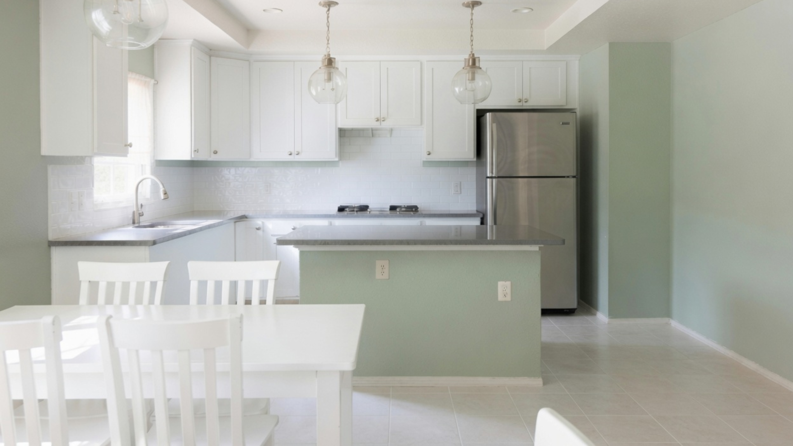 Small kitchen with white cabinets, pale mint walls and island, gray counters and stainless-steel appliances.
