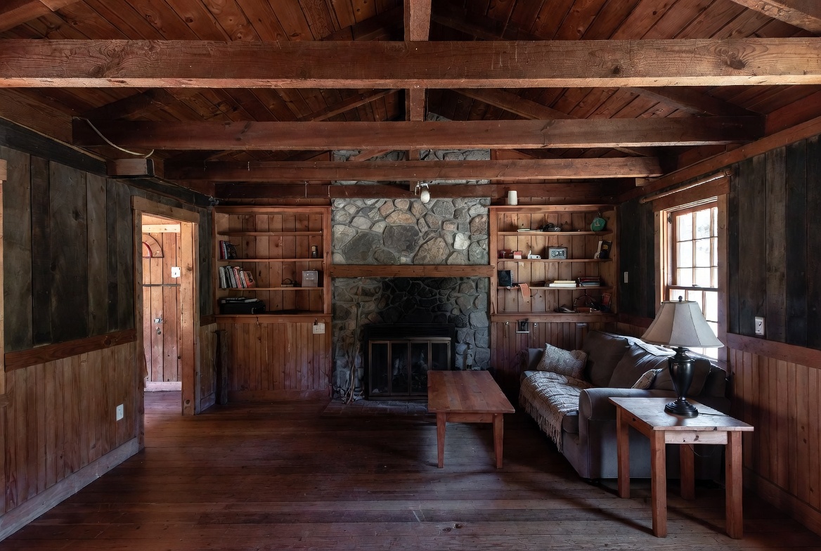Rustic room with exposed beams, wood walls, stone fireplace, and simple furniture.