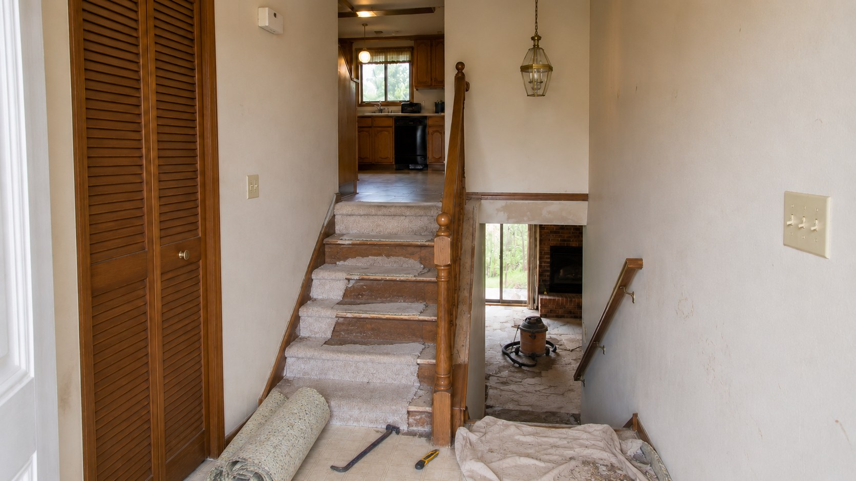 Split-level staircase during carpet removal with exposed wood treads, rolled padding, hand tools, and a shop vacuum.