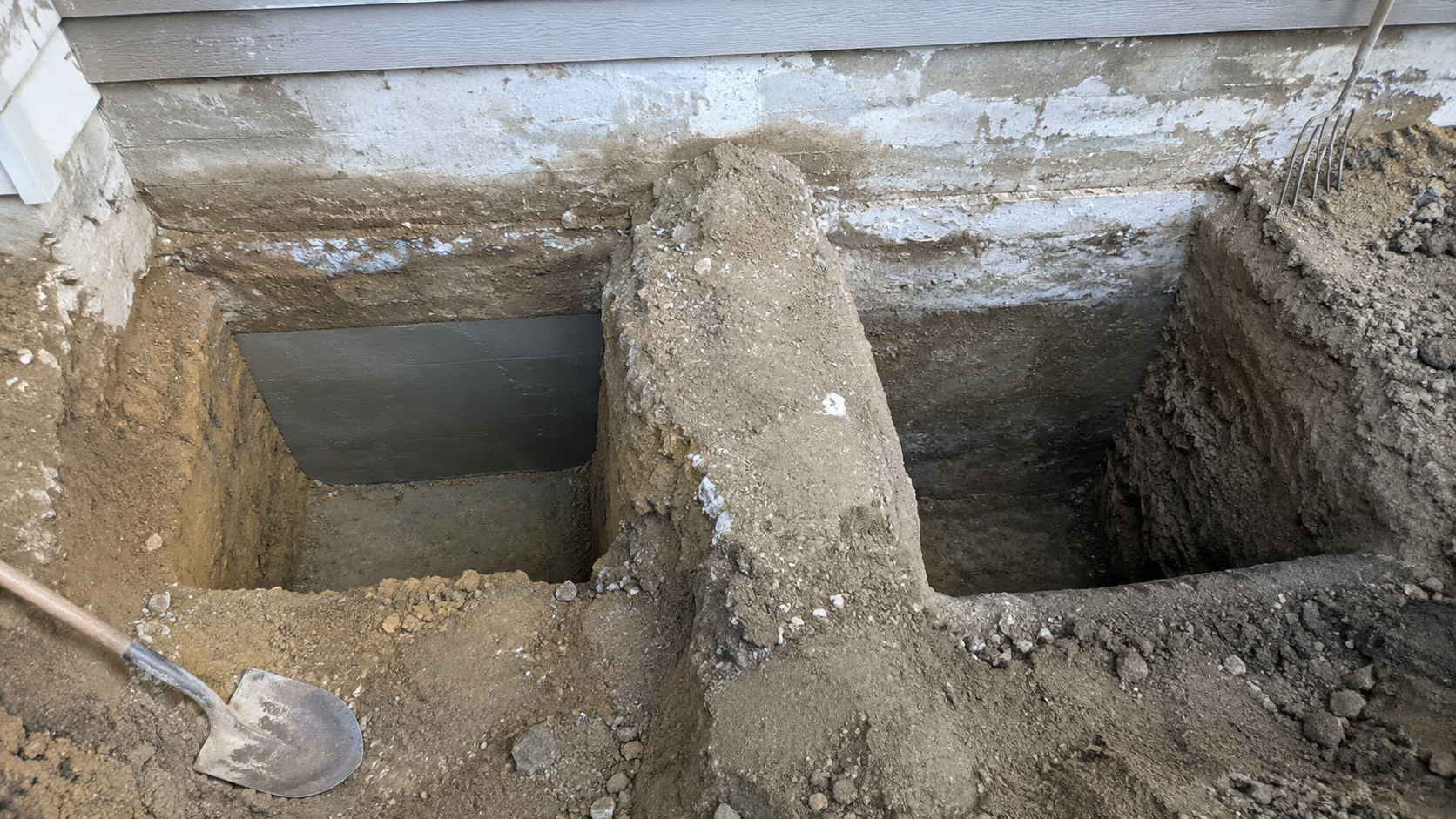 Completed and open underpinning bays separated by untouched soil beneath a foundation.
