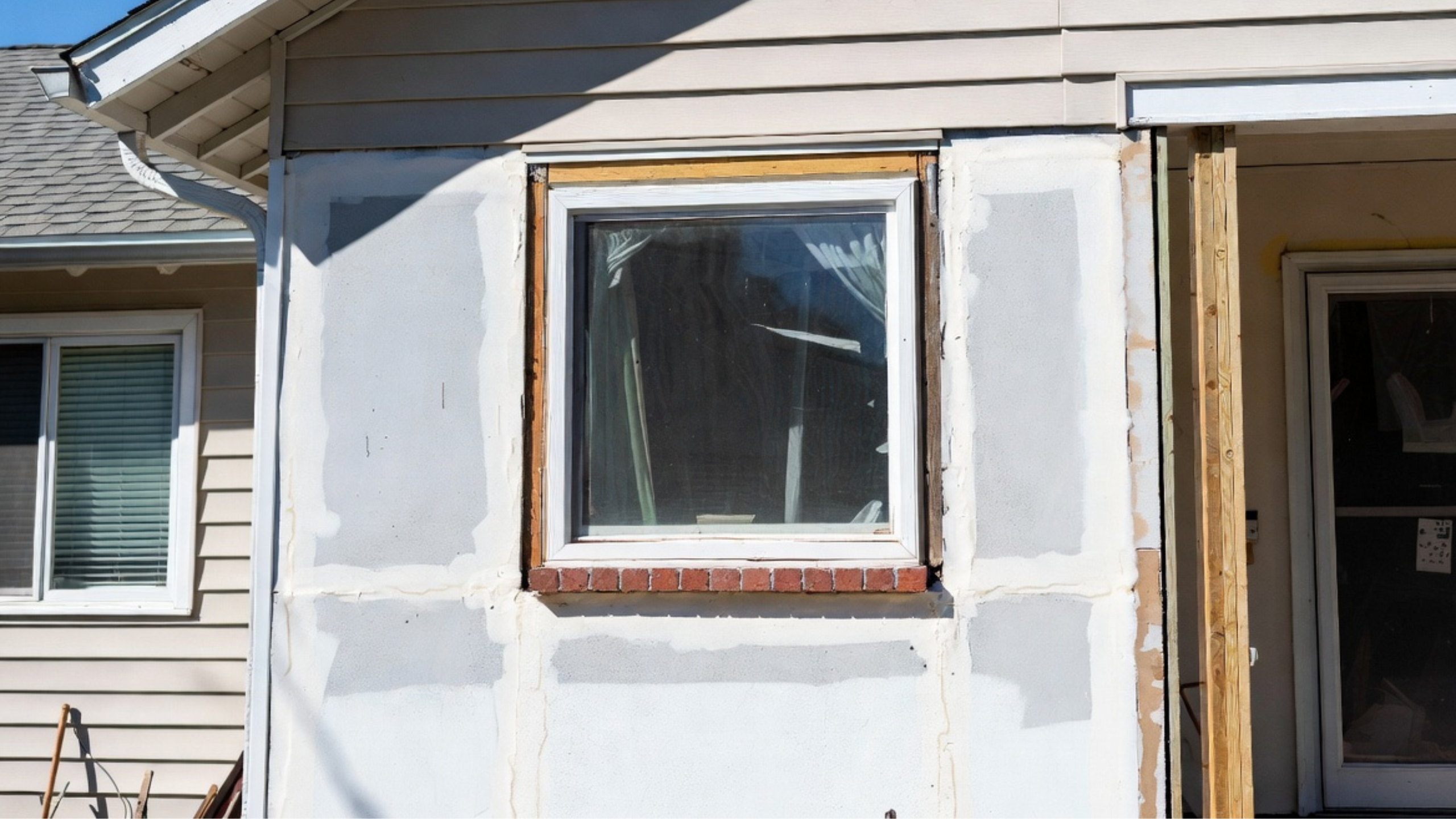 House wall with a replacement window, exposed framing, patched sheathing, and unfinished siding repair.