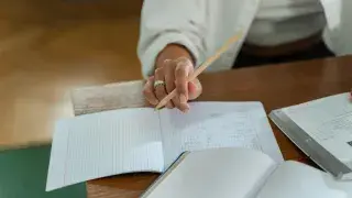 Student sitting on a wooden table, holding a pencil and concentrating on an architecture aptitude exercise.