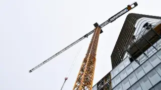 Modern glass building under construction with visible crane and materials.