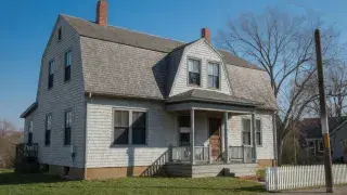 Showing Dutch Colonial Revival home with shingle siding, gambrel roof, and white picket fence in color.