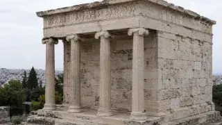 Ancient Greek Ionic columns with fluted shafts, carved capitals, weathered stone blocks, and a carved frieze.