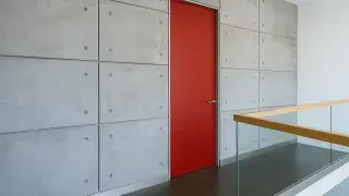 Modern loft interior with bold red door in concrete wall and glass railing.