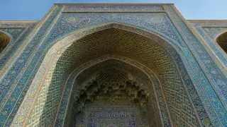 Upward view of an Islamic archway with muqarnas vaulting and blue geometric tile patterns.