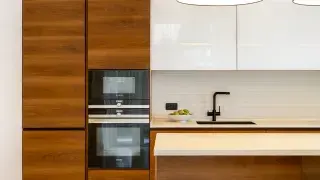 Modern kitchen with wood cabinets, white counters, and black faucet.