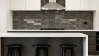 Modern kitchen with engineered stone benchtop, dark tiled splashback, and minimal design.