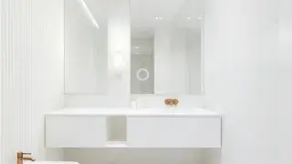 Modern all-white bathroom interior with marble walls, floating vanity, and soft diffused vanity lighting.