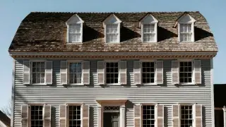 Colonial house with symmetrical facade, centered entrance, black shutters, and twin chimneys.