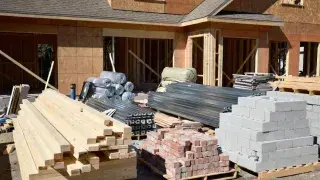Common building materials including lumber, brick, concrete block, steel, and insulation at a residential jobsite.