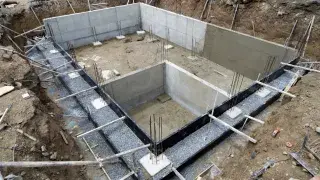 Concrete foundation walls with perimeter waterproofing and gravel drain zone.