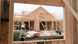 Construction manager reviewing plans at active house framing site for Construction Management.
