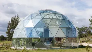 Glass dome house with visible glazing, curtains, and mixed transparent and opaque panels in a residential setting.