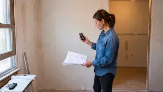 A handheld laser measure being used to check dimensions in a room under renovation.