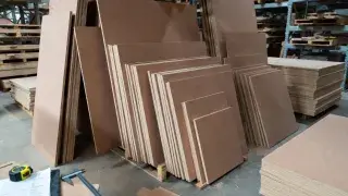 Stacked MDF sheets in various sizes and thicknesses on warehouse pallets with measuring tools.