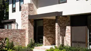 Modern house entry with brick accent walls, chimney, and restrained landscaping.