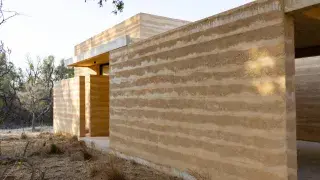 Finished rammed earth building with thick layered walls in a dry site setting.