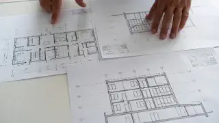 Person reviewing printed blueprint drawings on a table.