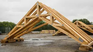 Wood scissor truss in a fabrication yard with sloped bottom chords and vaulted ceiling geometry.