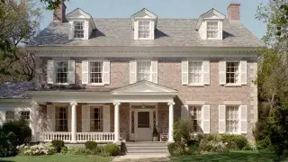 1910s Colonial Revival house with brick facade, dormers, shutters, and a classical front porch.