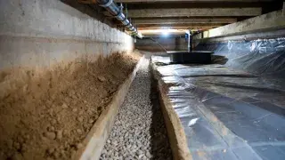 Crawl space perimeter drain trench and sump basin beside a ground vapor barrier.