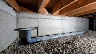 Crawl space drainage pipe in gravel bed connected to a sump basin beside a foundation wall.