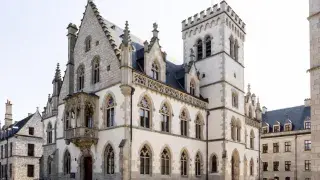Gothic civic building with pointed windows, stone walls, and a tall tower.