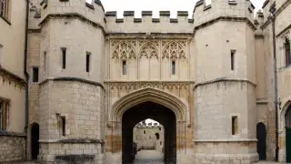 Gothic gatehouse with pointed arch entry, towered massing, and stone facade.