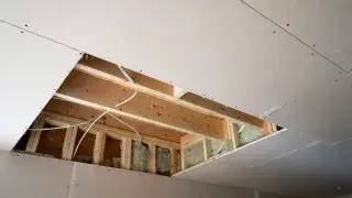 Opened ceiling showing joists, insulation, wiring, and drywall in a residential room.