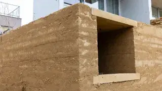 Rammed earth wall corner showing wall thickness above a concrete base.