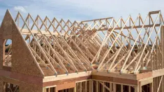 Residential roof trusses under construction with sloped framing and open sky above.