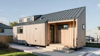 Tiny home on wheels with timber cladding, dormer loft, and small porch.