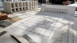Architectural worktable with a gridded floor plan, facade study, massing model, material samples, ruler, and tracing paper.