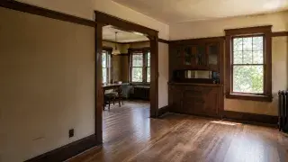 Original 1920s Craftsman interior with dark woodwork, built-in cabinet, radiator, and worn floors.