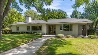 Updated 1960s ranch house exterior with low roofline, painted brick, vertical siding, simple entry, broad front windows, and restrained landscaping.