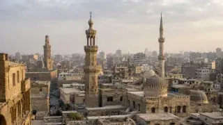 Historic Islamic city skyline with mosque minarets rising above domes, courtyards, rooftops, and narrow streets.