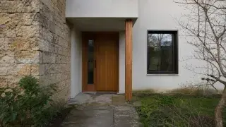 House entry with rough stone, smooth stucco, wood door, glass, and worn paving.