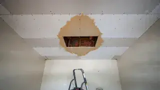 Wet ceiling drywall with a small cutout exposing the leak area above the damaged patch.