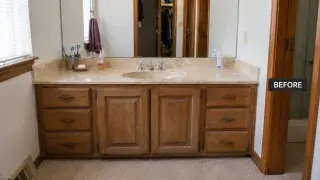 1980s bathroom vanity with oak cabinet, yellow cultured marble top, large mirror, dated faucet, and carpeted floor.
