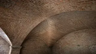 Close view of a brick groin vault showing the diagonal intersection of two curved vault surfaces.