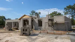 Concrete block house under construction with CMU walls, rebar, scaffolding, and jobsite materials.