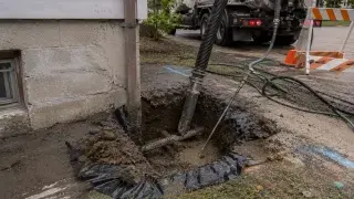 Hydrovac excavation exposing a supported buried utility beside an existing residential foundation.
