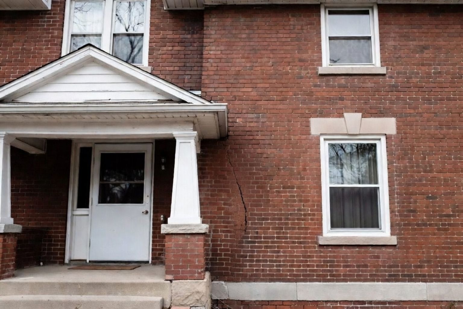 Brick house exterior with a diagonal settlement crack running toward the foundation.