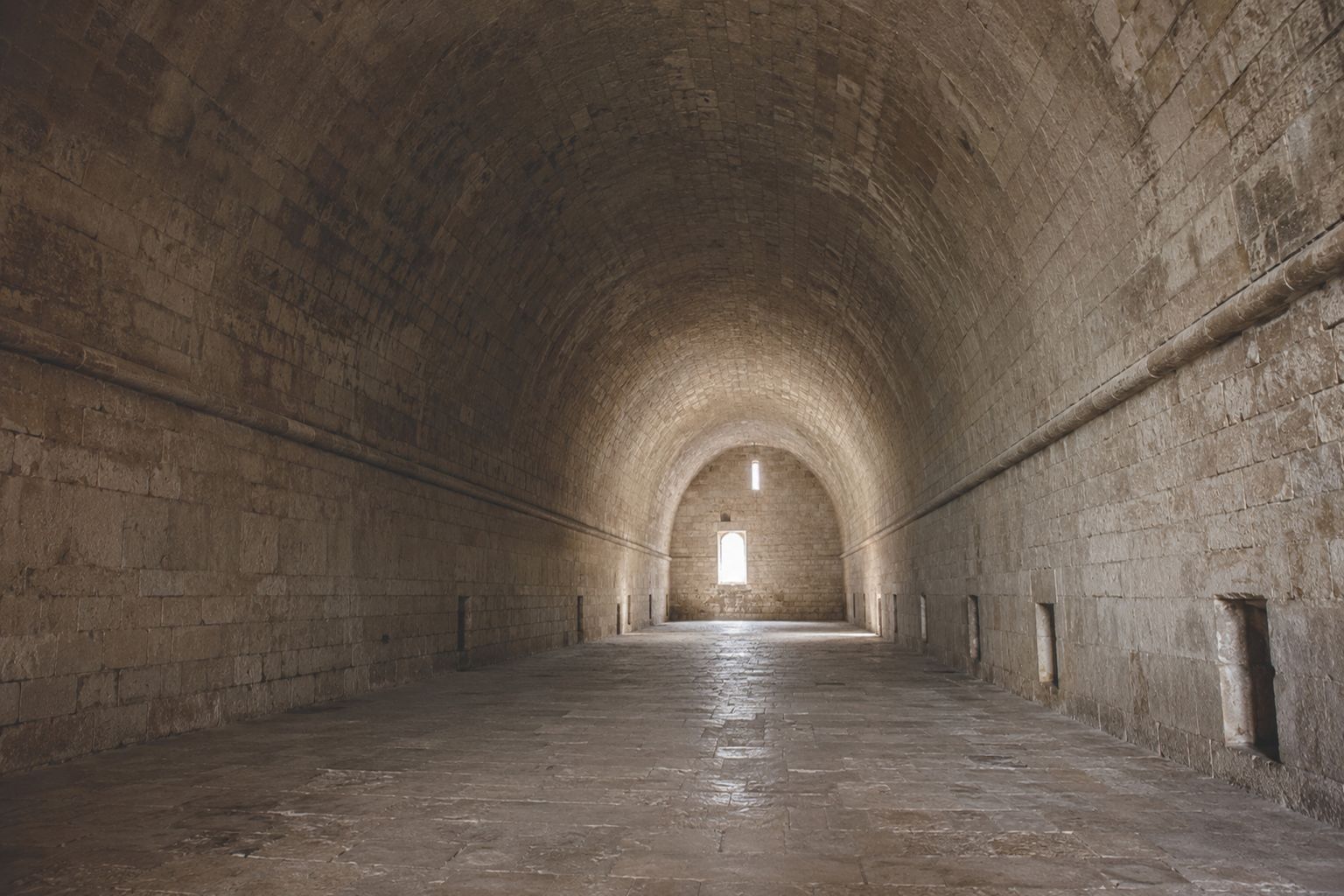 Long stone hall covered by a continuous barrel vault above thick masonry side walls.