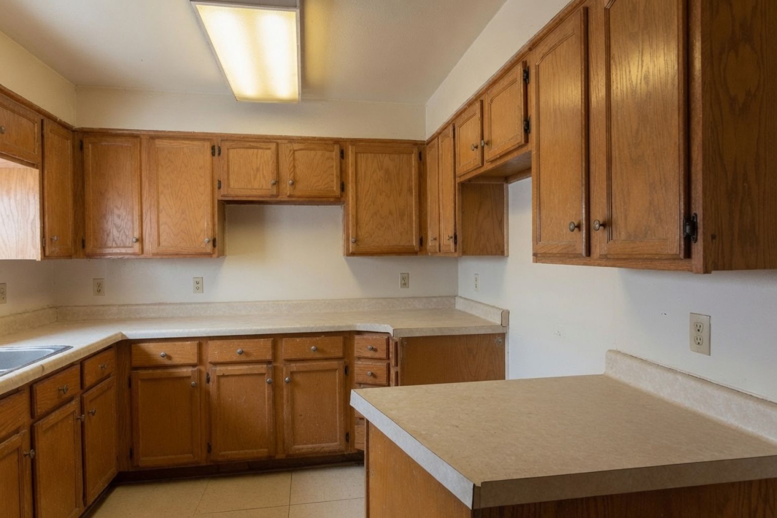 Dated empty kitchen with oak cabinets, laminate counters, and fluorescent lighting.