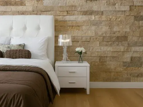 Modern bedroom interior featuring a natural stone accent wall, white headboard, and minimalist decor.