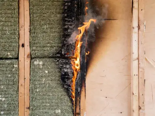 Hemp insulation in an open stud wall showing flame exposure, surface charring, and smoke.